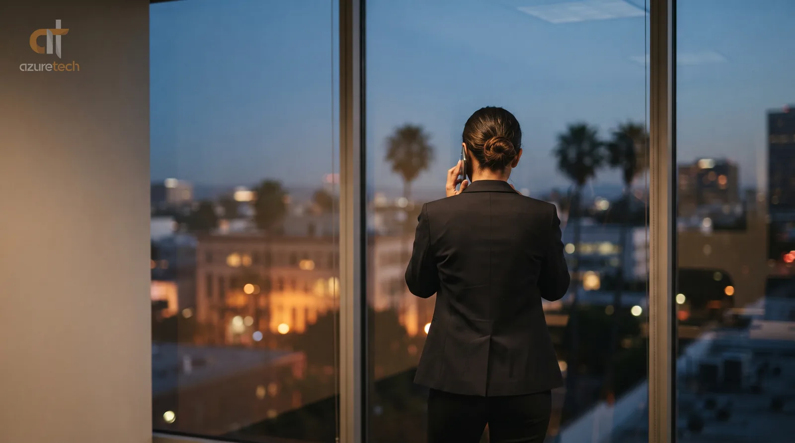 An attorney standing at an office window at dusk, phone to the ear, waiting